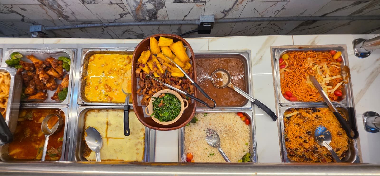 Overhead view of the Goianeiro buffet: chicken, stews, rice, beans, pasta, fried cassava with torresmo