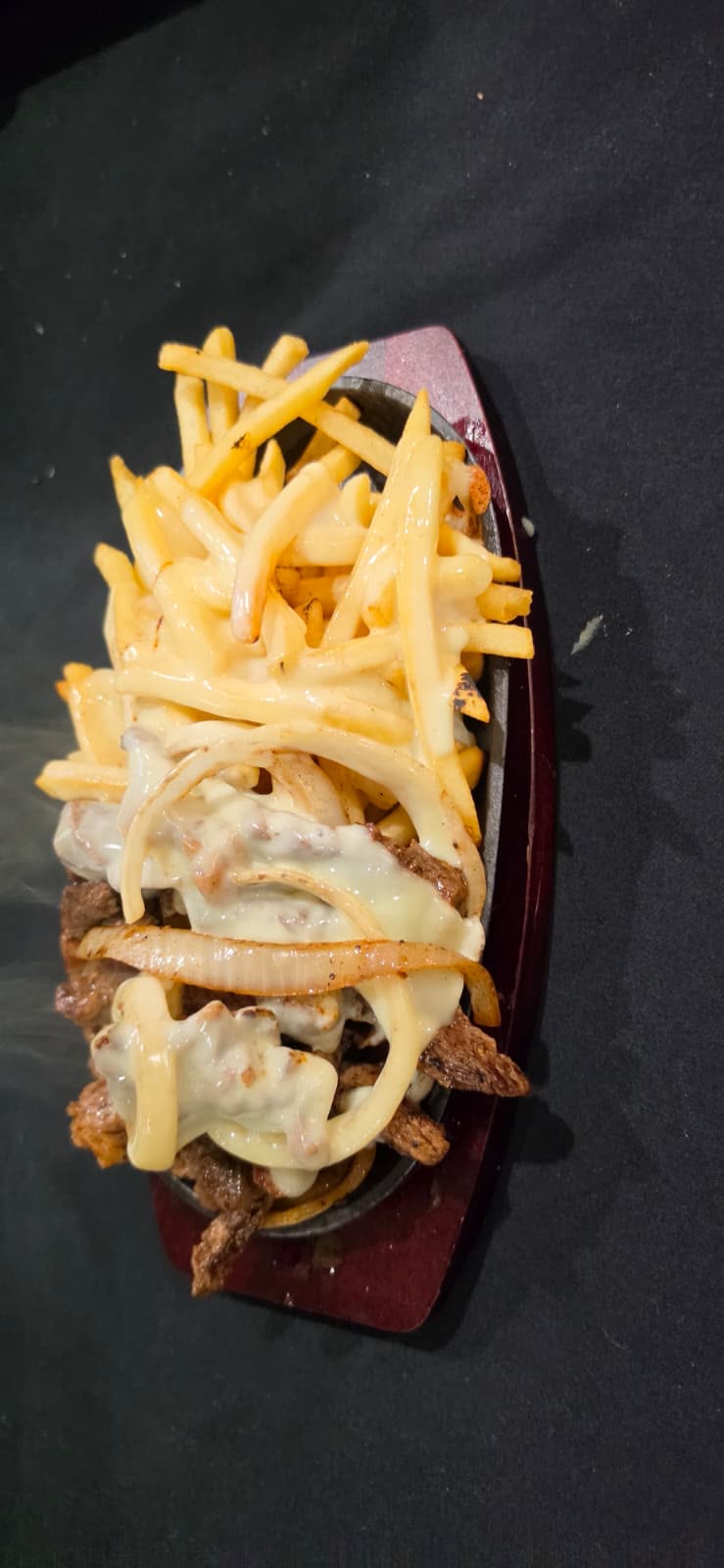 Sizzling cast-iron plate of sliced steak, onions and fries under melted cheese