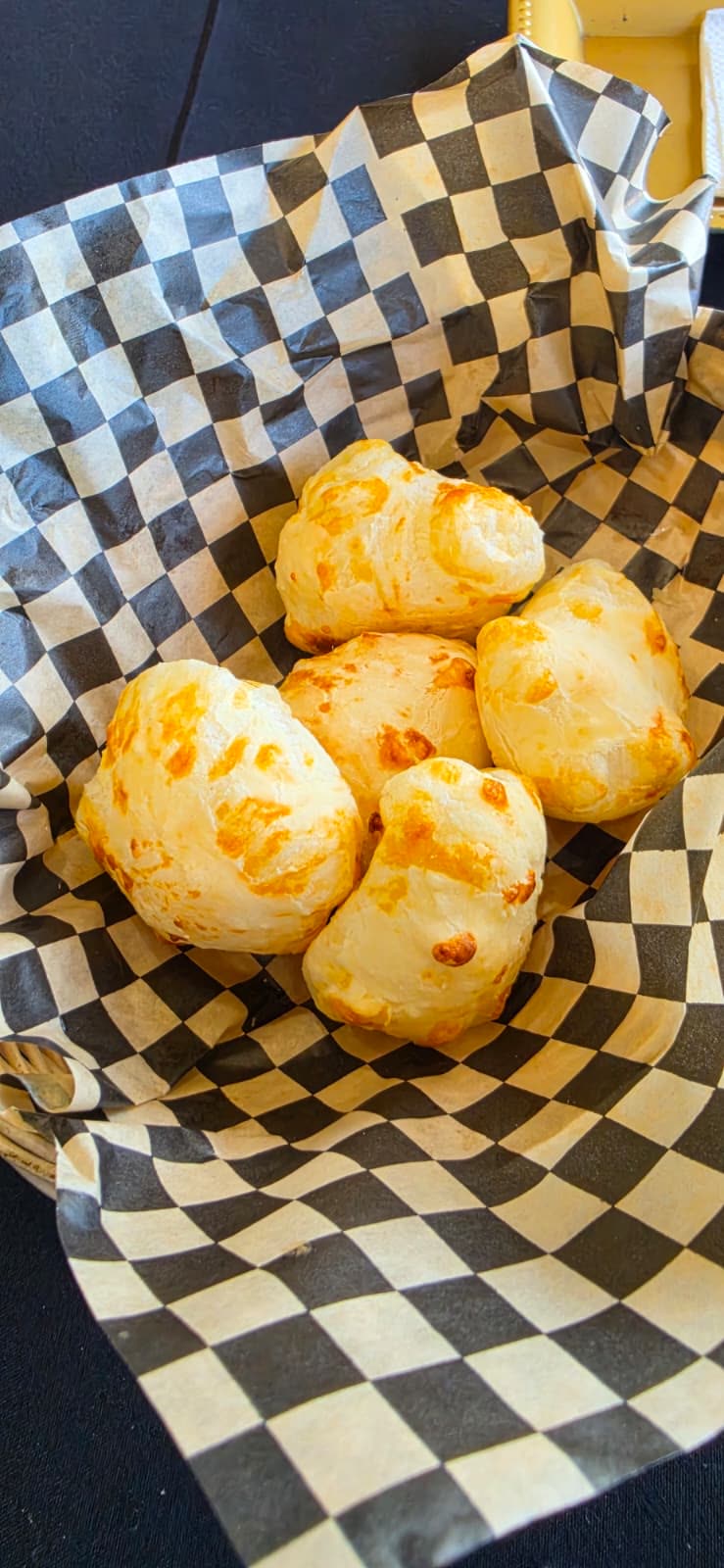 Basket of freshly baked pão de queijo on checkered paper